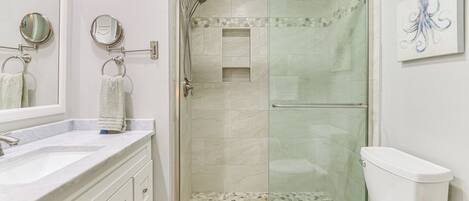 Un baño con cabina de ducha de vidrio, inodoro blanco y tocador con espejo y argollas para toallas.