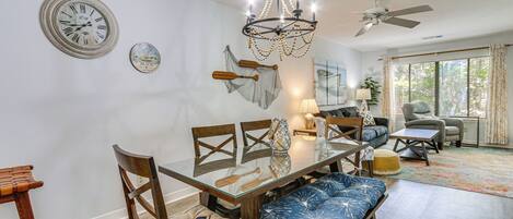 A dining area with a glass table, wooden chairs, a chandelier, and a ceiling fan.