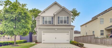 A two-story house with a garage, a wooden fence, and a tree in the front yard.