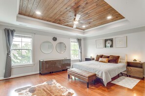 Une chambre avec un plafond en bois, un lit doté d ’une tête de lit, un banc, une table de chevet et une grande fenêtre.