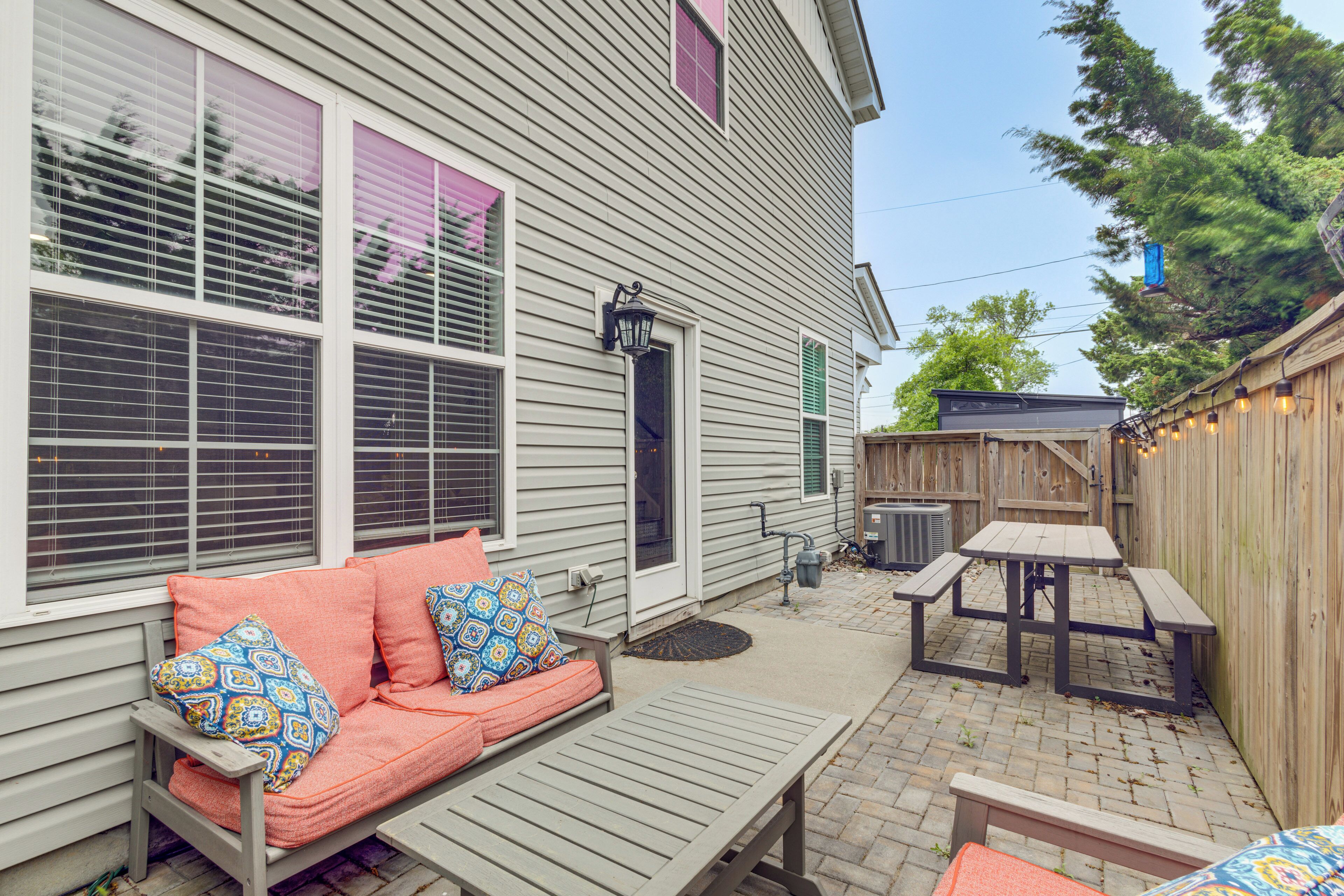 A patio with a wooden bench, a wooden table, and a sofa with patterned cushions.