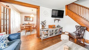 Een woonkamer met een bank, een salontafel, een aan de muur bevestigde televisie en een trap.