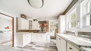 Een ruime keuken met witte kasten, een groot eiland en uitzicht op de omgeving door de ramen.