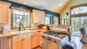 A modern kitchen with wooden cabinets, a stainless steel stove, and large windows offering views of the outdoors. - 24-0139 Cabin in Fairplay: Close to Trails! (Fairplay)