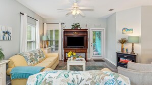 A living room with a sofa, a coffee table, a TV, a ceiling fan, and a door with a window.