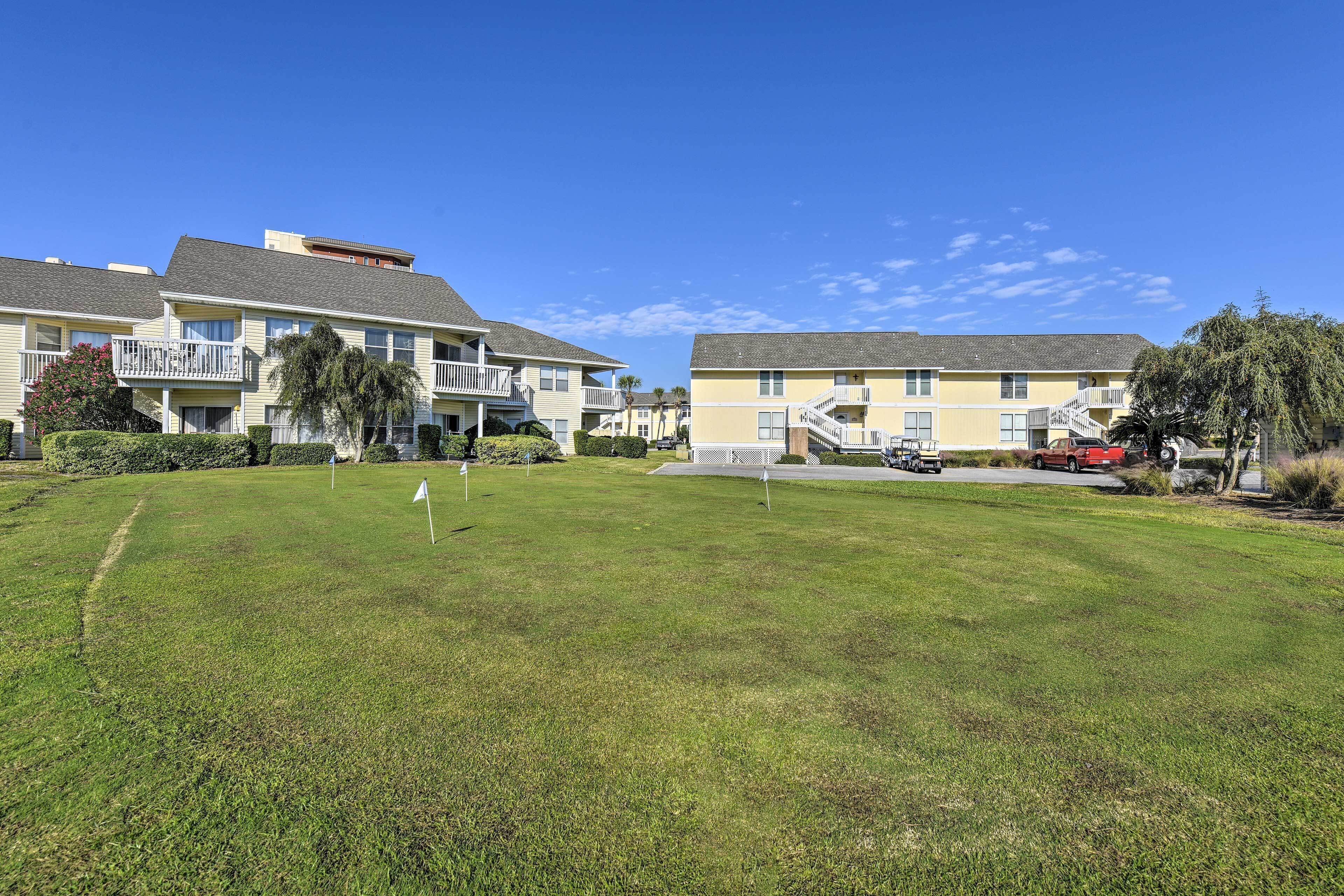 A residential area with two-story buildings, a grassy lawn, and a red vehicle parked near the buildings.