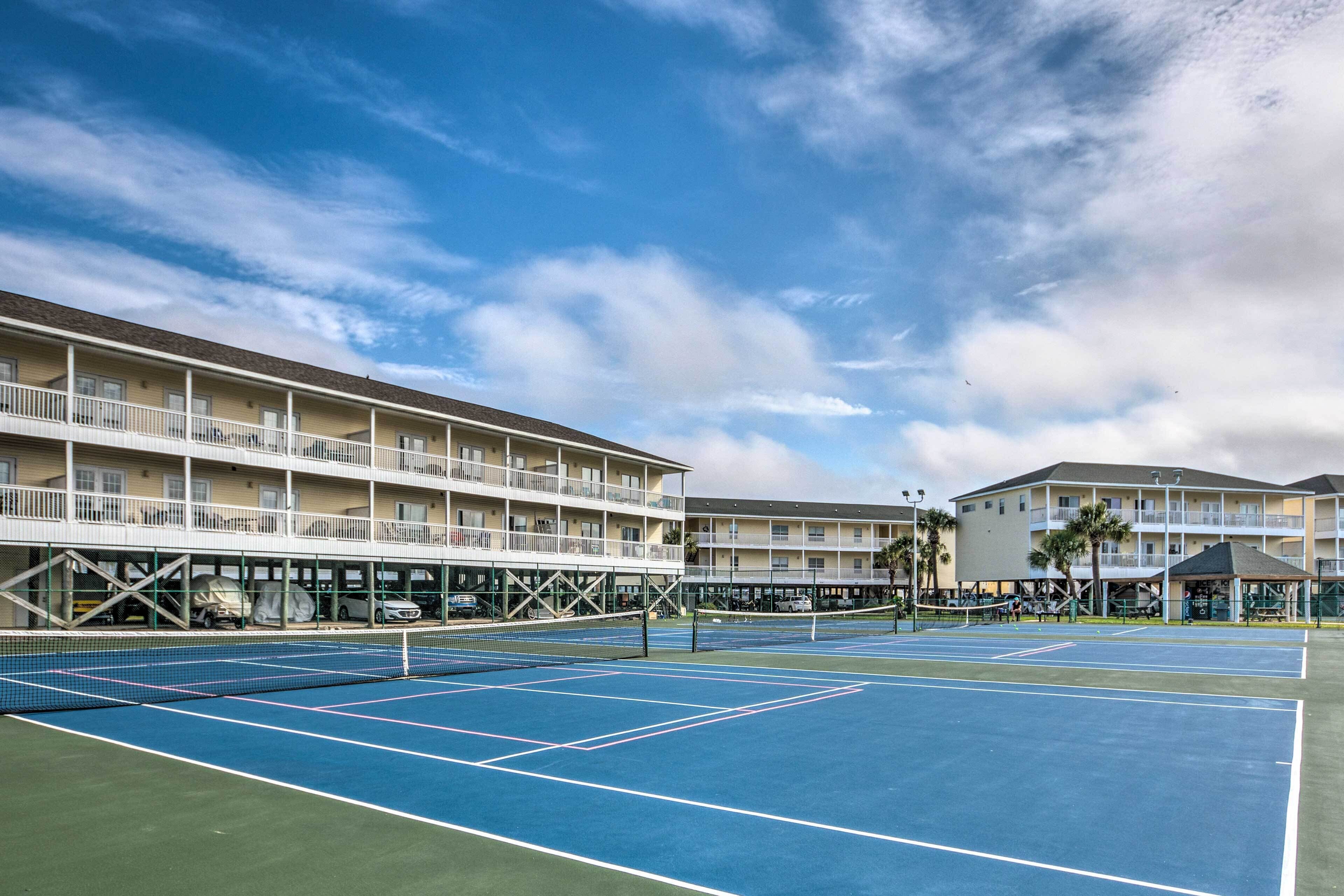 A tennis court with a net in the middle, surrounded by a multi-story building with balconies.
