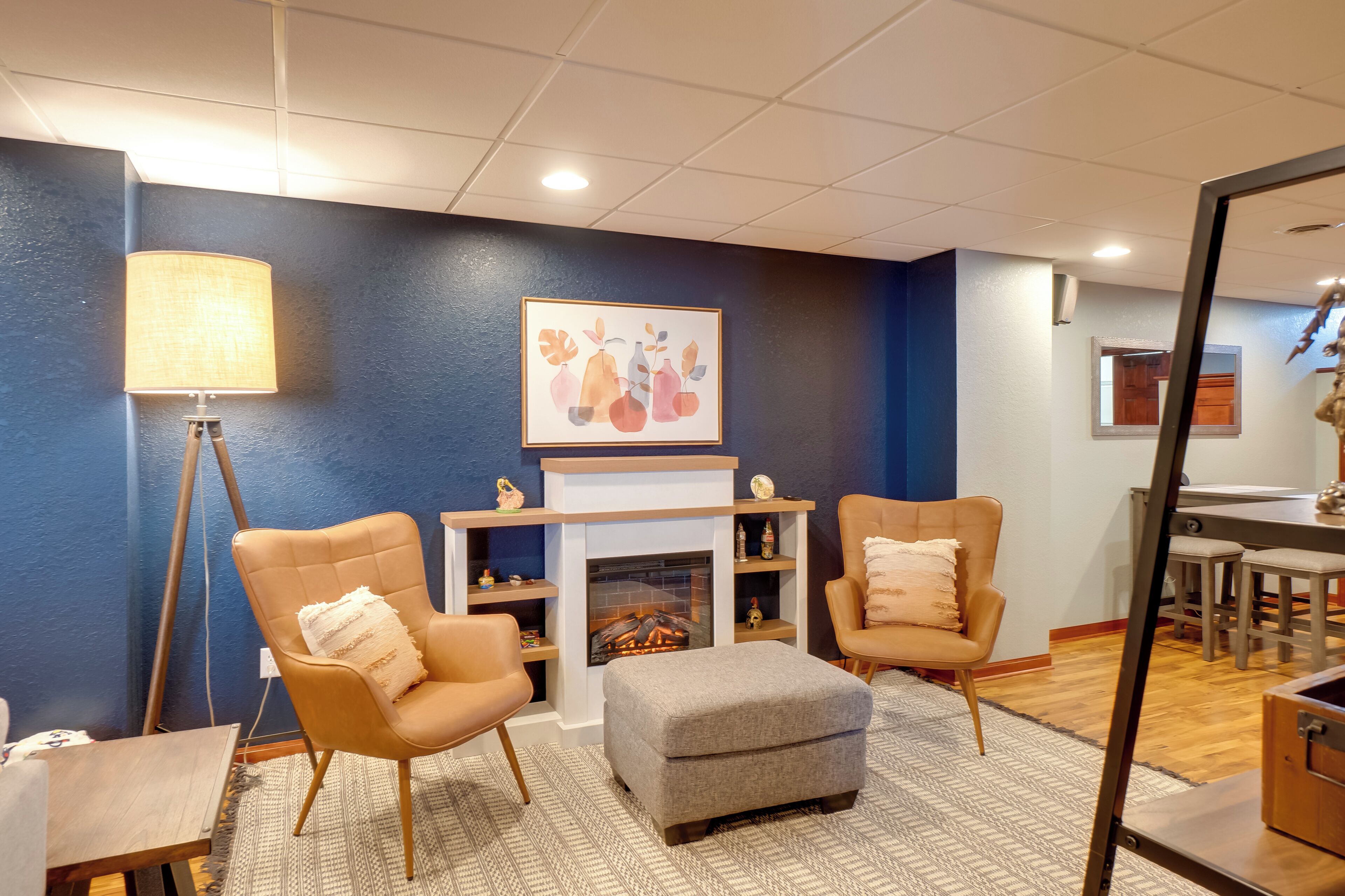 A cozy room with two armchairs, a grey ottoman, a fireplace, and a framed artwork on the wall.