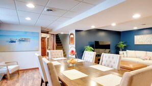 A modern dining area with a wooden table, white upholstered chairs, and a blue accent wall with a painting. - Cozy Milwaukee Apartment w/ Deck, 2 Mi to Airport! (Milwaukee)