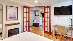 A hotel room with a bed, a desk with a computer, a TV, a fireplace, and a view of the hallway. - Cozy Milwaukee Apartment w/ Deck, 2 Mi to Airport! (Milwaukee)