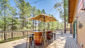 En träveranda med en bardisk, utomhusmöbler och utsikt över den omgivande skogen.
