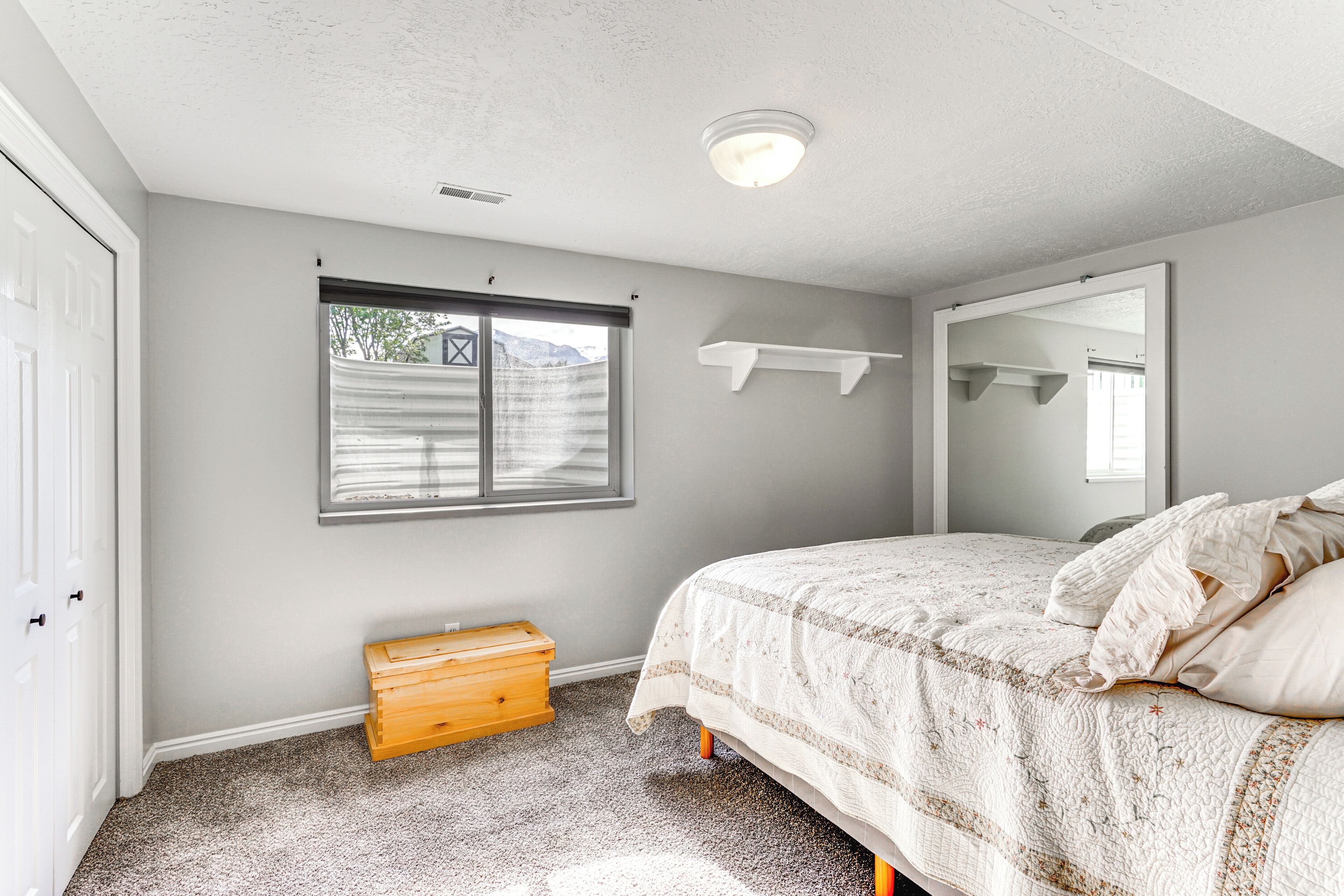 A bedroom with a bed, a window, a wooden chest, and a mirror on the wall.
