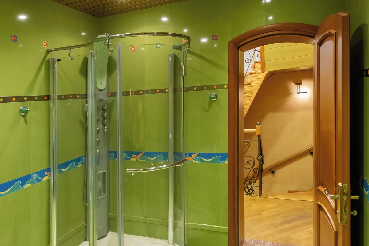 A shower enclosure with a glass door, a wooden staircase, and a green tiled wall.