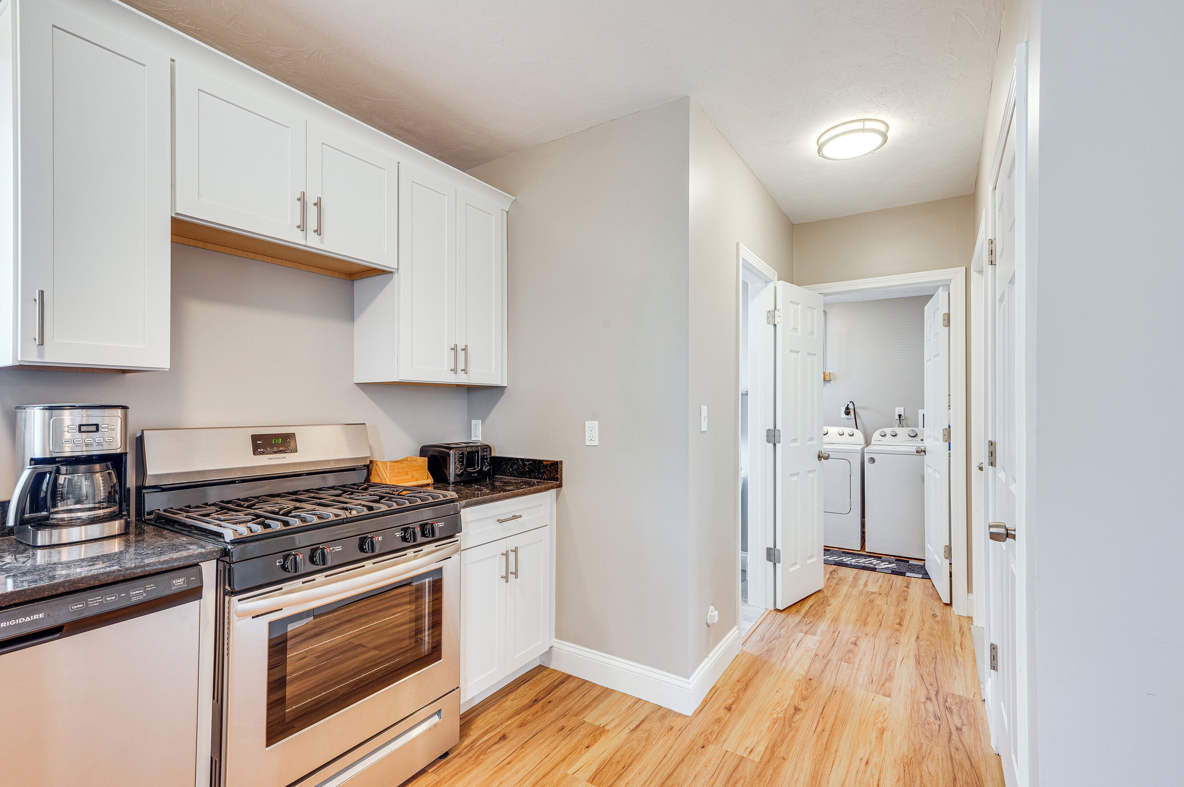 A modern kitchen with white cabinets, stainless steel appliances, and a wooden floor.