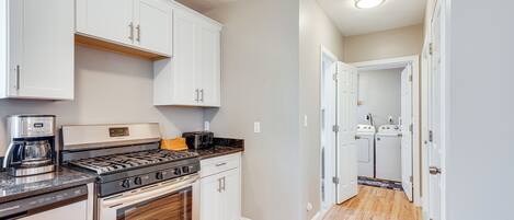 A modern kitchen with white cabinets, stainless steel appliances, and a wooden floor.
