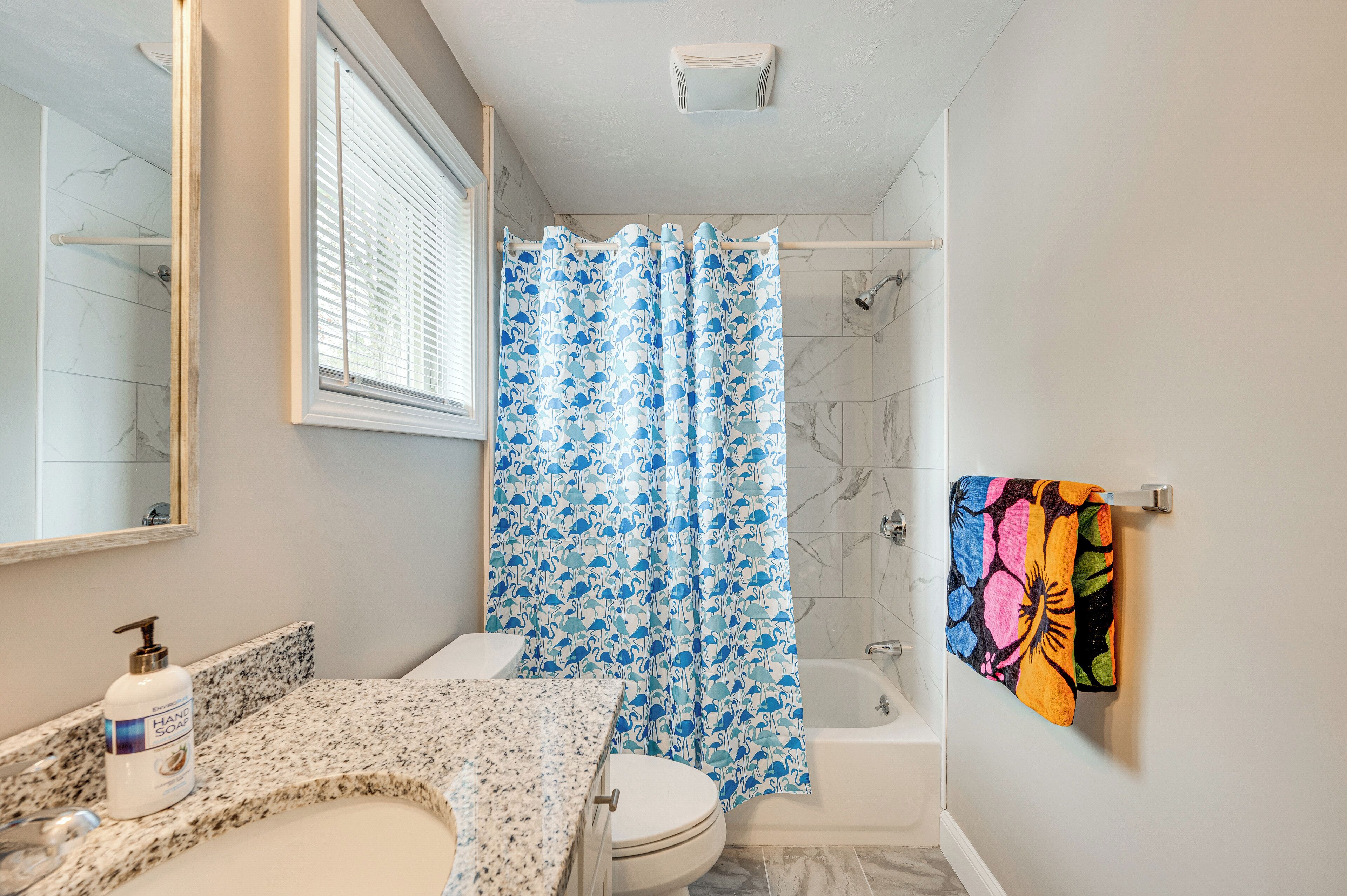 A bathroom with a marble sink, a toilet, a shower with a blue floral shower curtain, and a towel rack with a colorful towel.