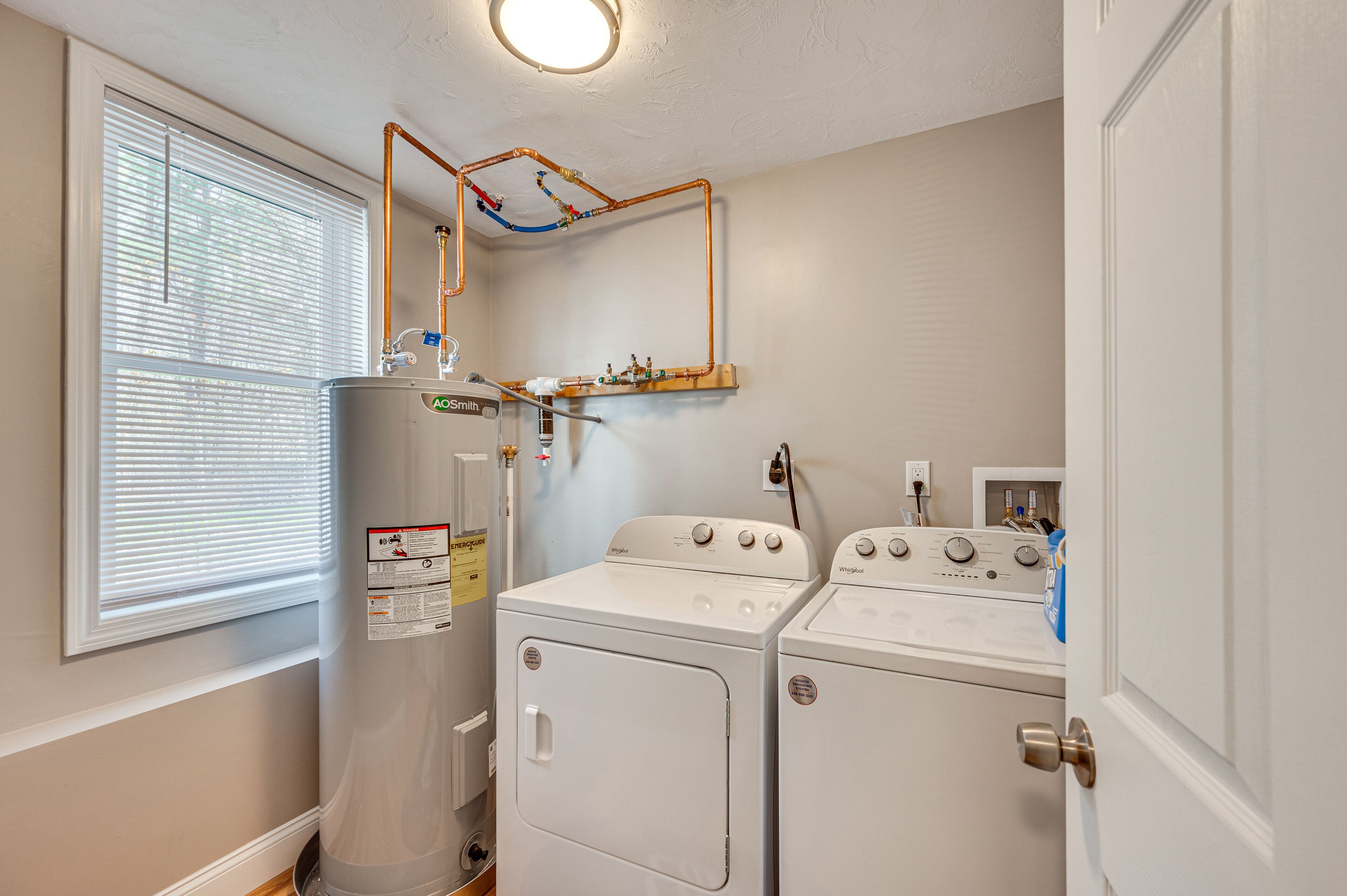 A laundry room with a washer and dryer, a water heater, and a window with blinds.