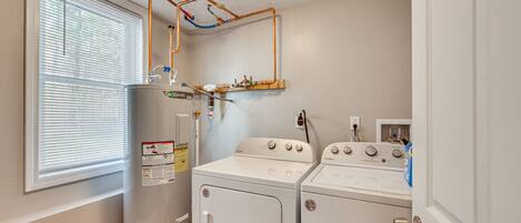 A laundry room with a washer and dryer, a water heater, and a window with blinds.