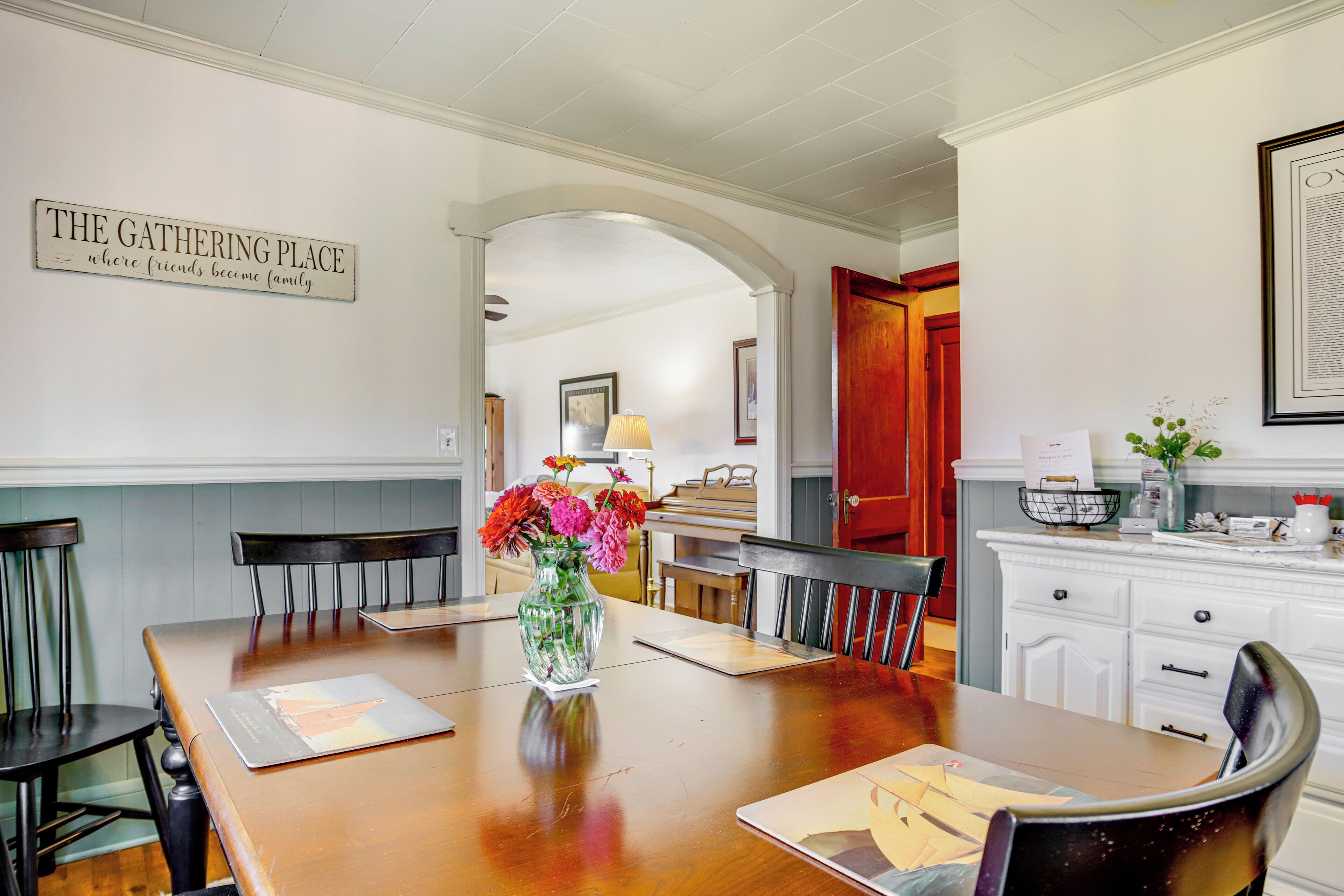 A dining area with a wooden table, chairs, a vase with flowers, and a sign on the wall.