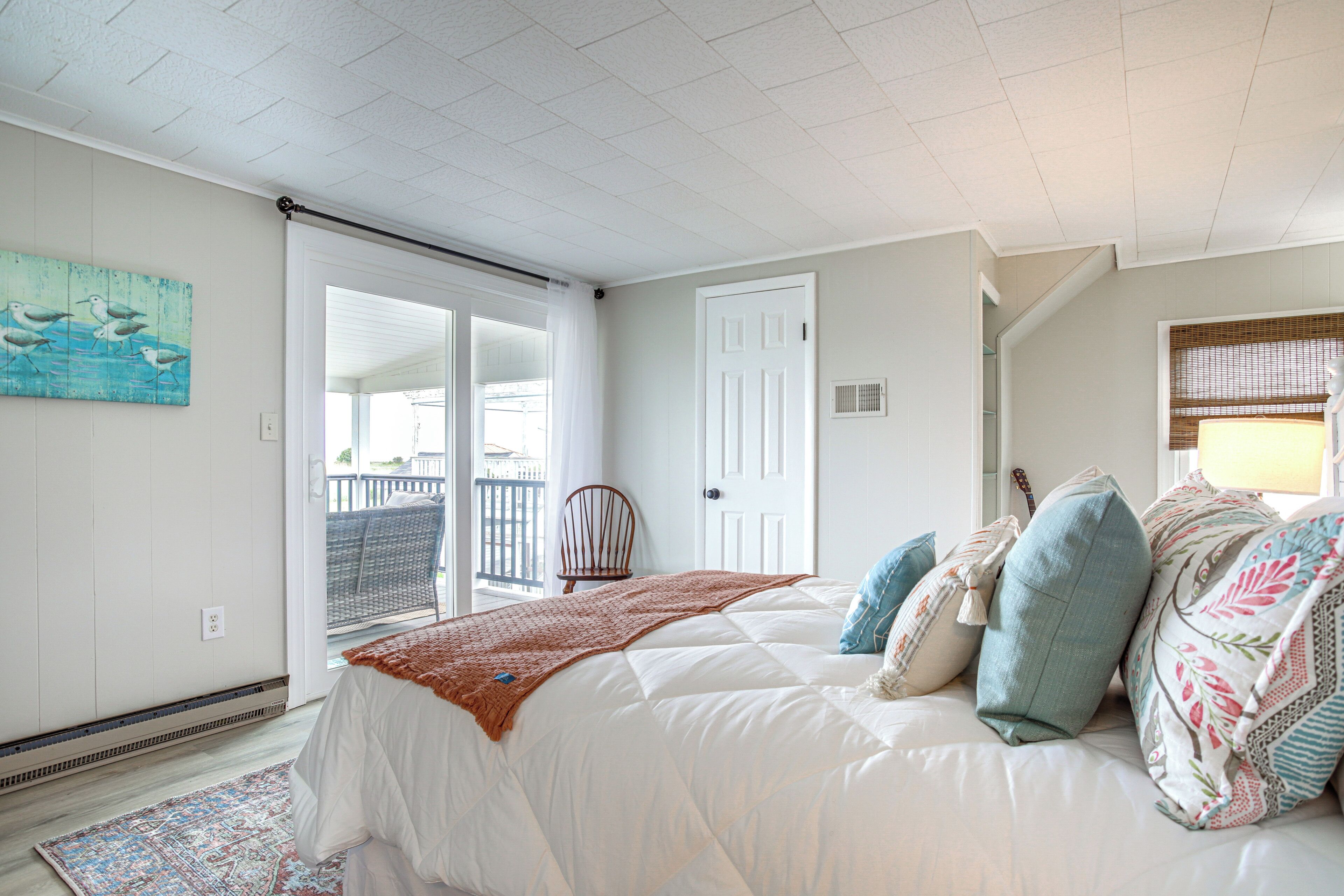 A bedroom with a large bed, a door, a chair, and a view of the outside.
