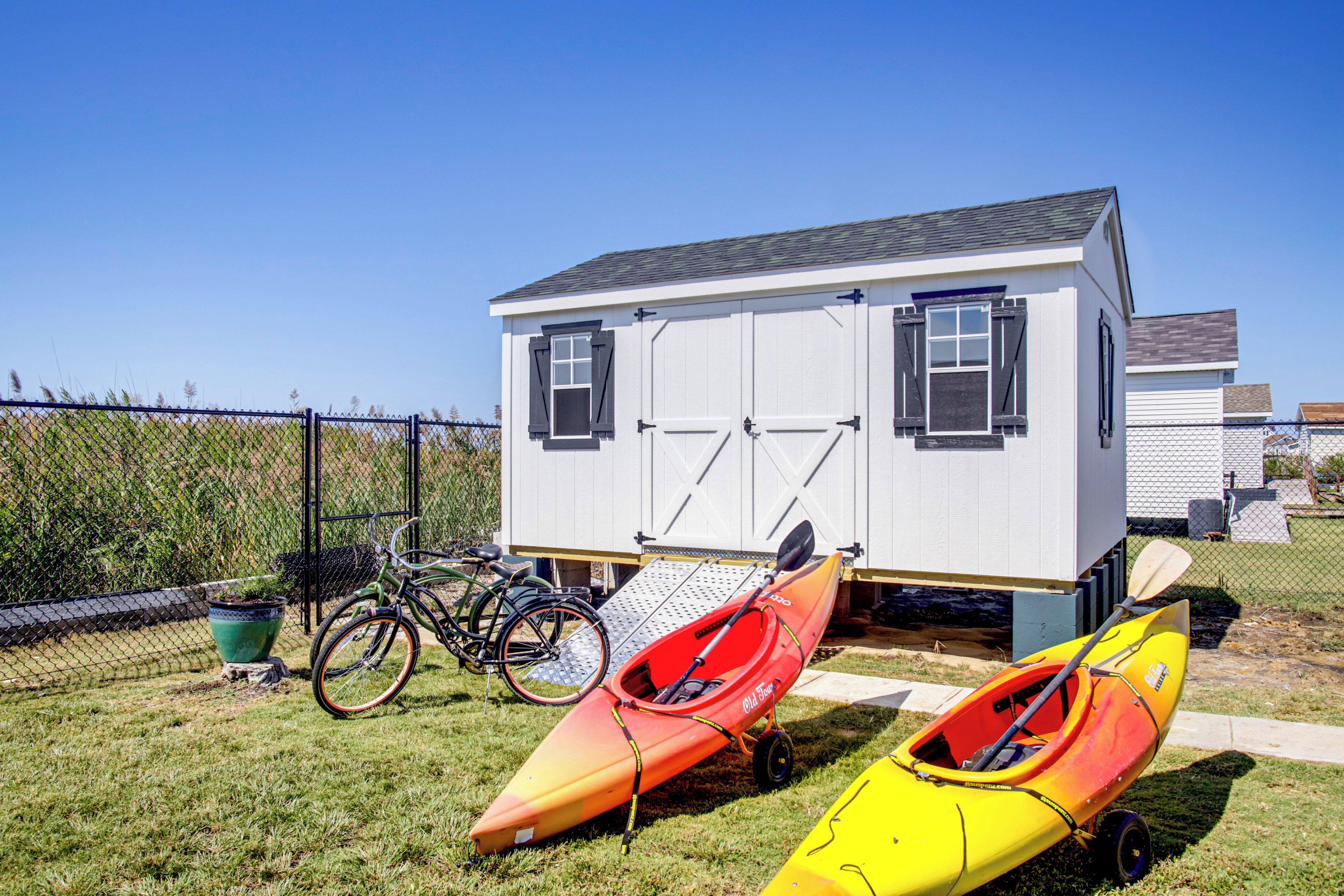 A small white building with a garage door, two kayaks, and a bicycle.