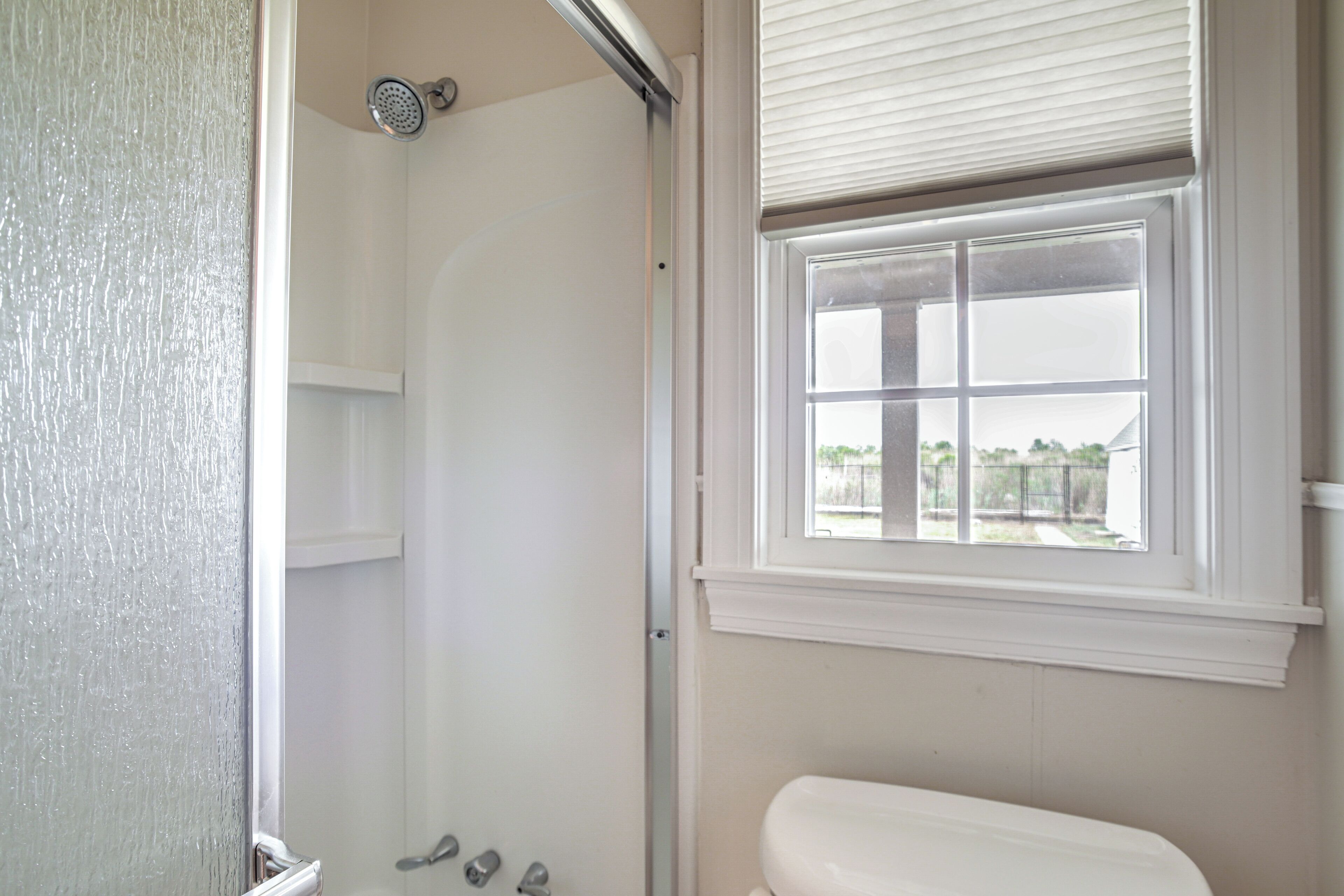 Een badkamer met douche, toilet en raam.