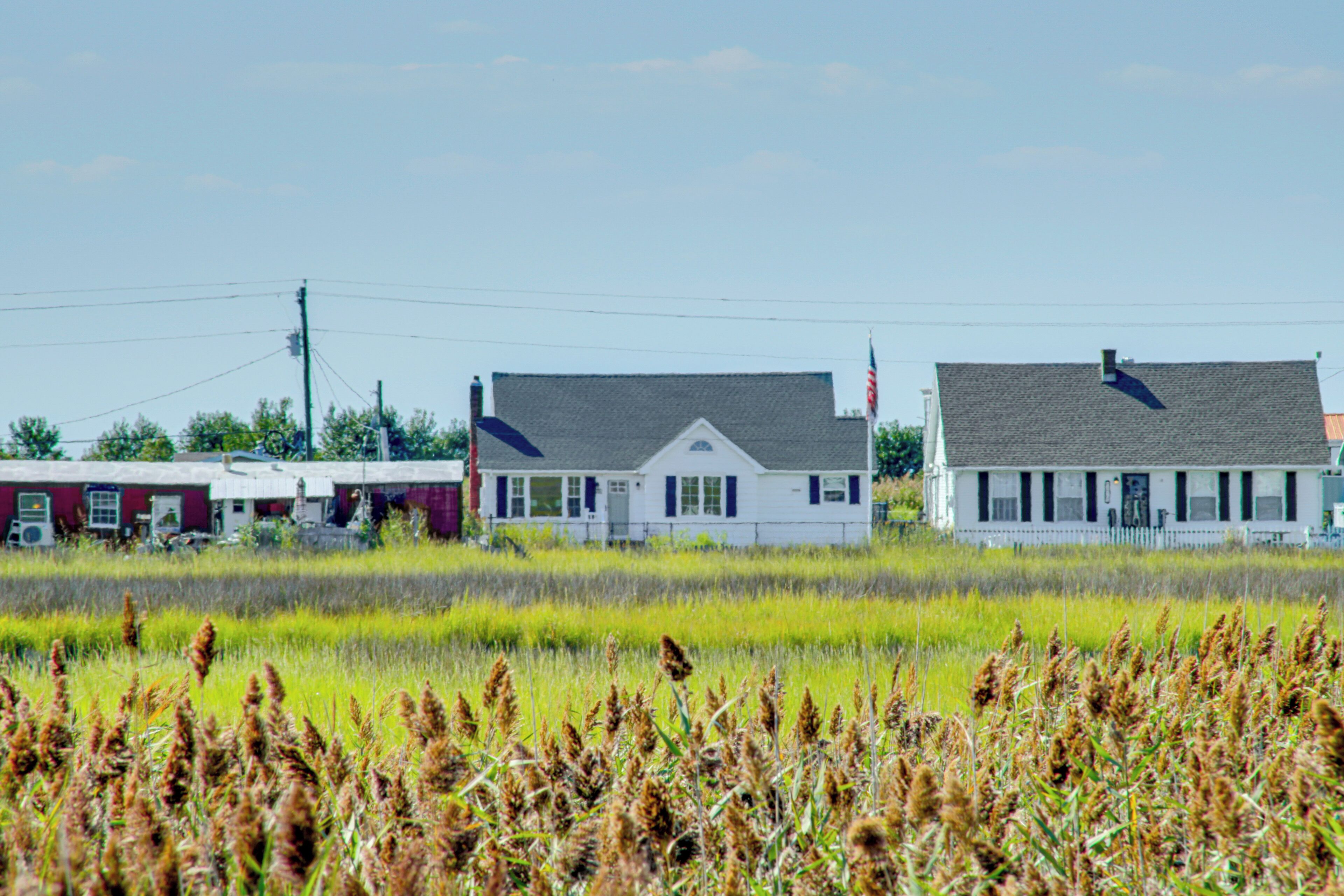 A white building with a grey roof, surrounded by fields and other buildings.