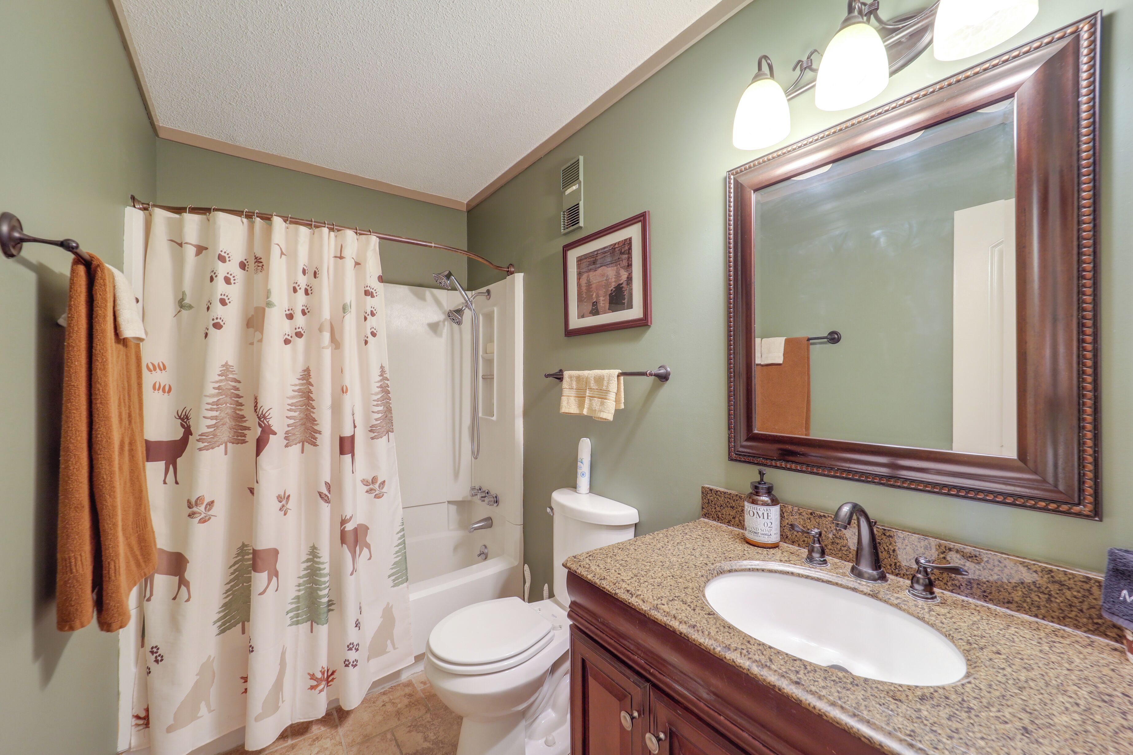 A bathroom with a shower curtain, toilet, sink, and mirror.