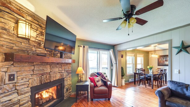 A cozy living room with a stone fireplace, a leather sofa, and a dining area with wooden flooring. - Furnished Deck + Resort Perks: Beech Mtn Retreat! (Banner Elk)
