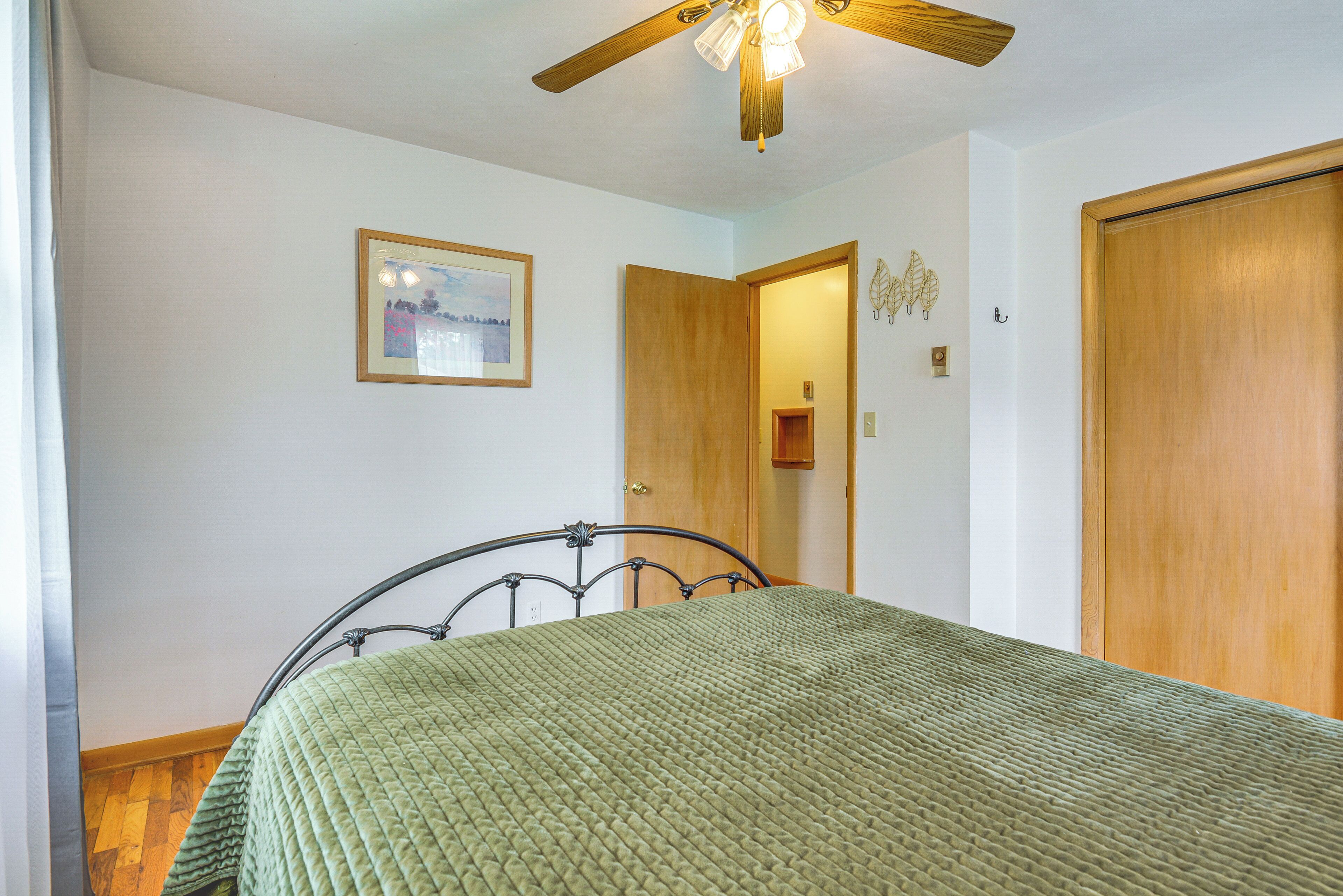 Un dormitorio con una cama, un ventilador de techo, una puerta de madera y un cuadro enmarcado en la pared.