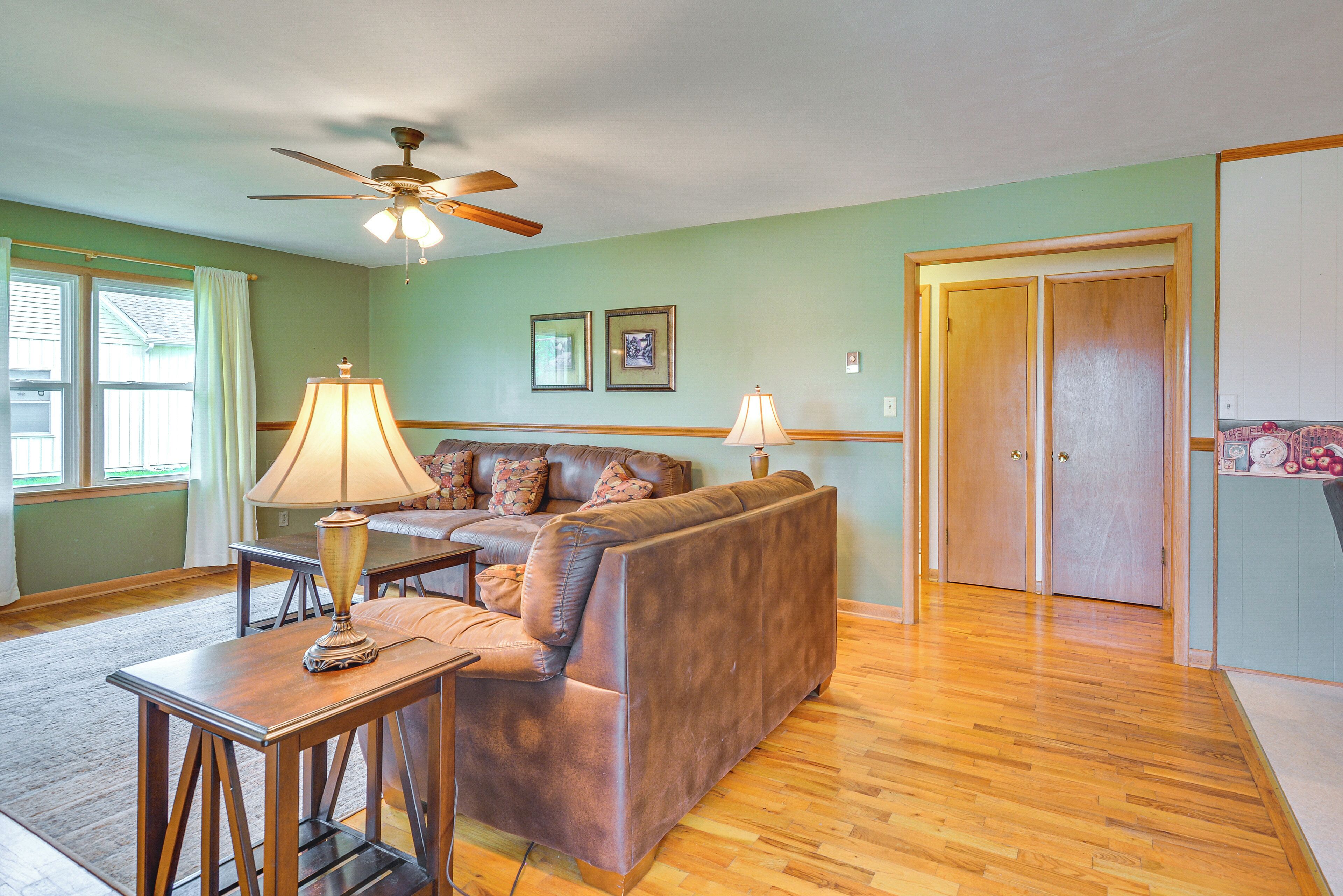 A living room with a brown leather sofa, a wooden coffee table, a ceiling fan, and a wooden door.