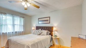 A bedroom with a bed, a ceiling fan, a nightstand with a lamp, and a framed picture on the wall. - Walk to Restaurants: Stockton Home w/ Game Room (Stockton)