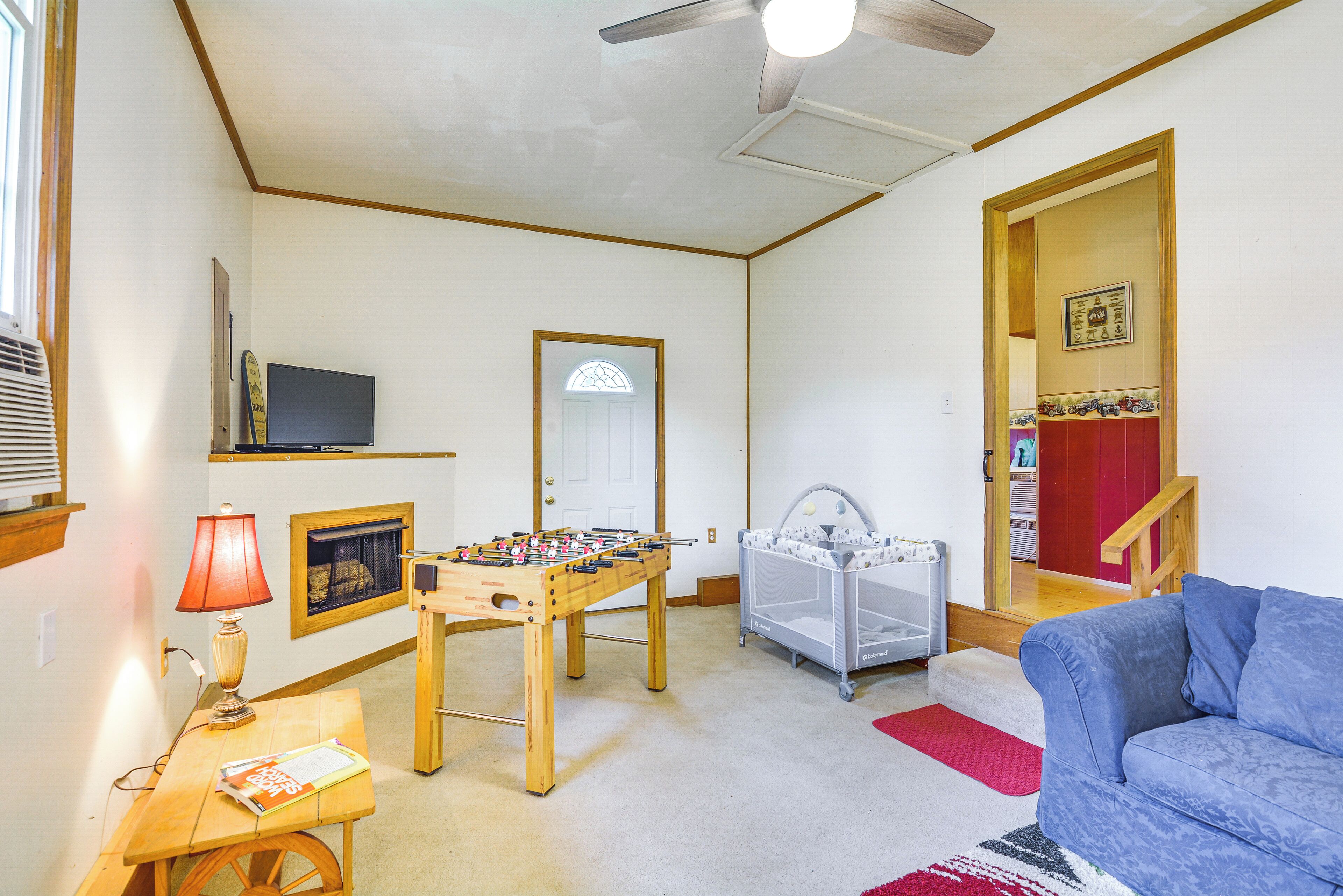 A living room with a foosball table, a television, a baby playpen, and a blue couch.