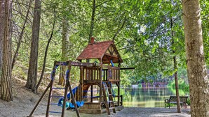 A wooden play structure with a slide and swings, surrounded by trees and a bench near a body of water. - Game Room & Patio: Picturesque Home in Sonora (Sonora)