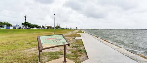 A coastal walkway with a signboard, grassy area, and a view of the sea.