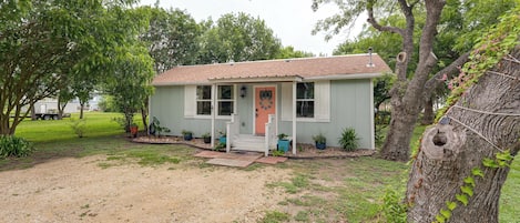 A single-story house with a front porch, a small driveway, and a large tree to the right.