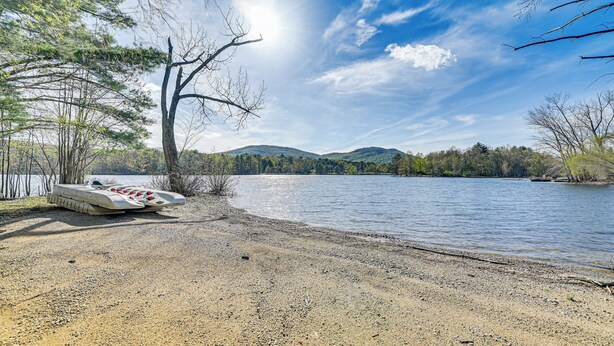 A lakeside scene with a boat docked on the shore, surrounded by trees and hills in the background. - Fire Pit + Beach Access: Quiet Northville Retreat (Northville)