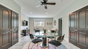 A spacious room with a glass-top table surrounded by chairs, a ceiling fan, and a large window. - Fire Pit + Beach Access: Quiet Northville Retreat (Northville)