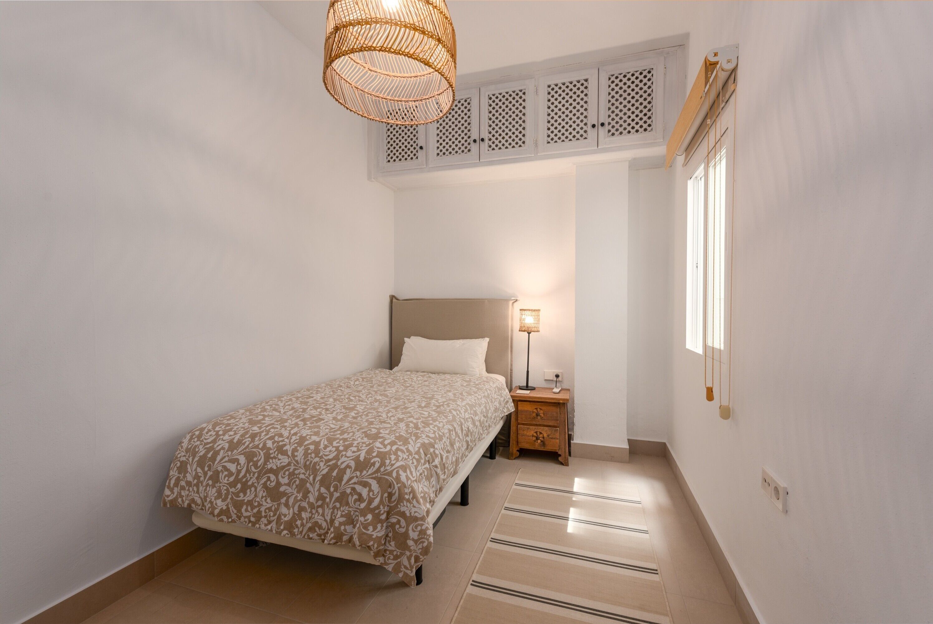 Une chambre à coucher comprenant un lit, une table de chevet, une lampe, un ventilateur de plafond et une fenêtre.