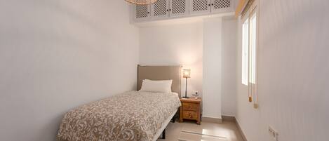 Une chambre à coucher comprenant un lit, une table de chevet, une lampe, un ventilateur de plafond et une fenêtre.