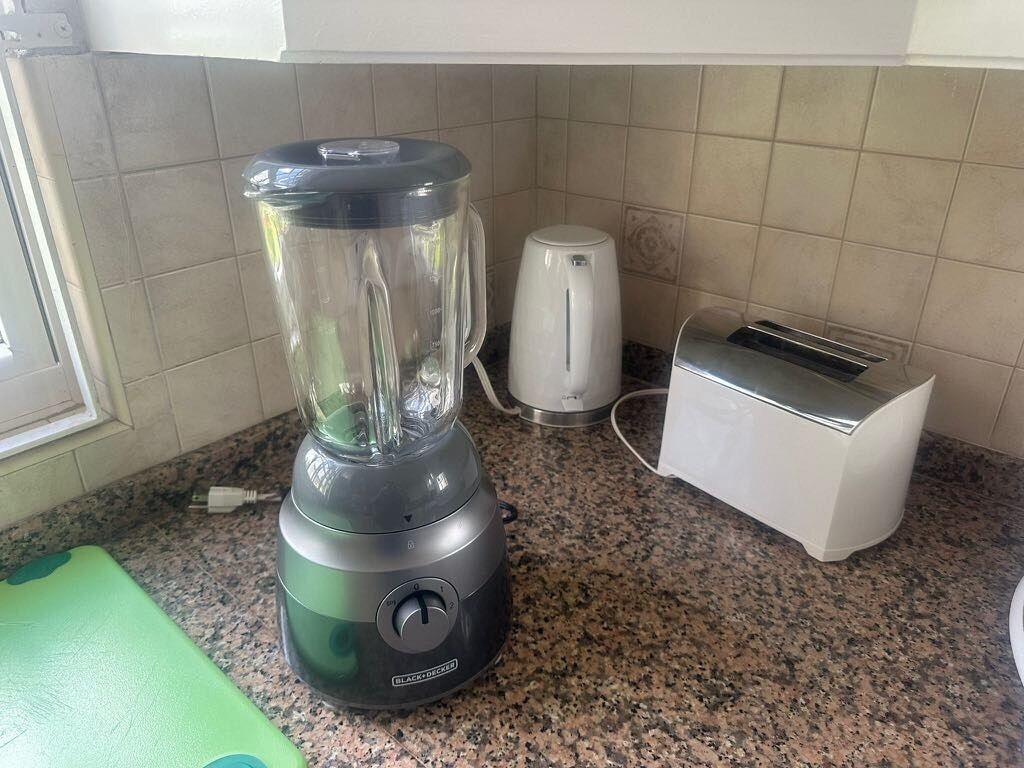 A kitchen with a blender, a toaster, and a green cutting board.