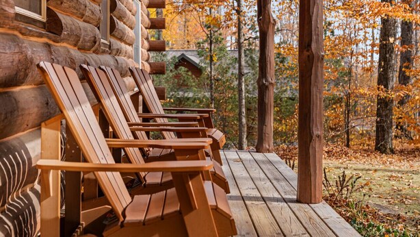 Een houten terras met Adirondack-stoelen en een blokhut op de achtergrond.