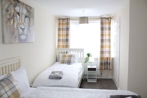 A bedroom with a bed, a nightstand, a lamp, and a window with curtains. - Captivating 3-bed House in Newcastle Upon Tyne (Newcastle-upon-Tyne)