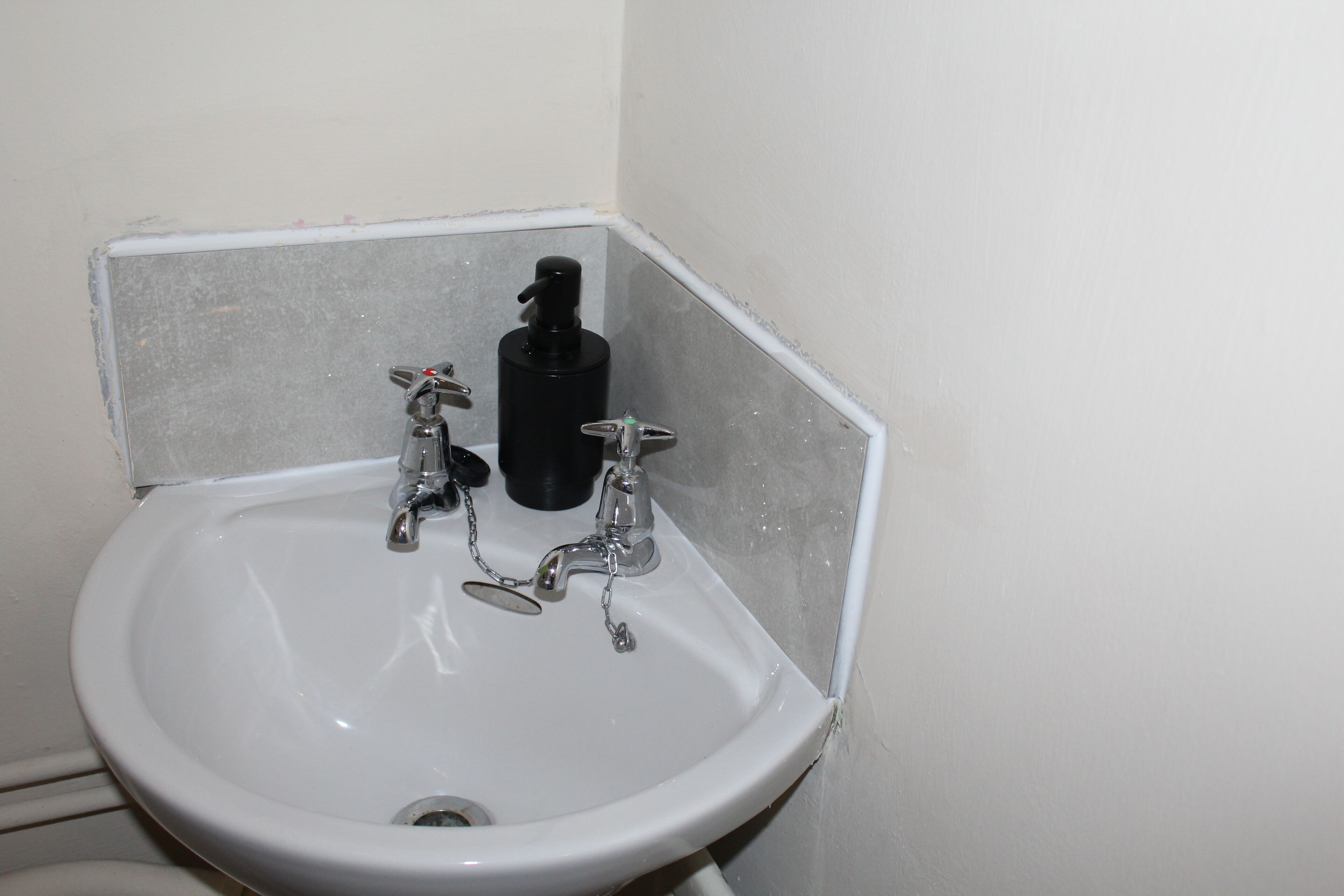 A corner bathroom sink with two faucets and a soap dispenser.