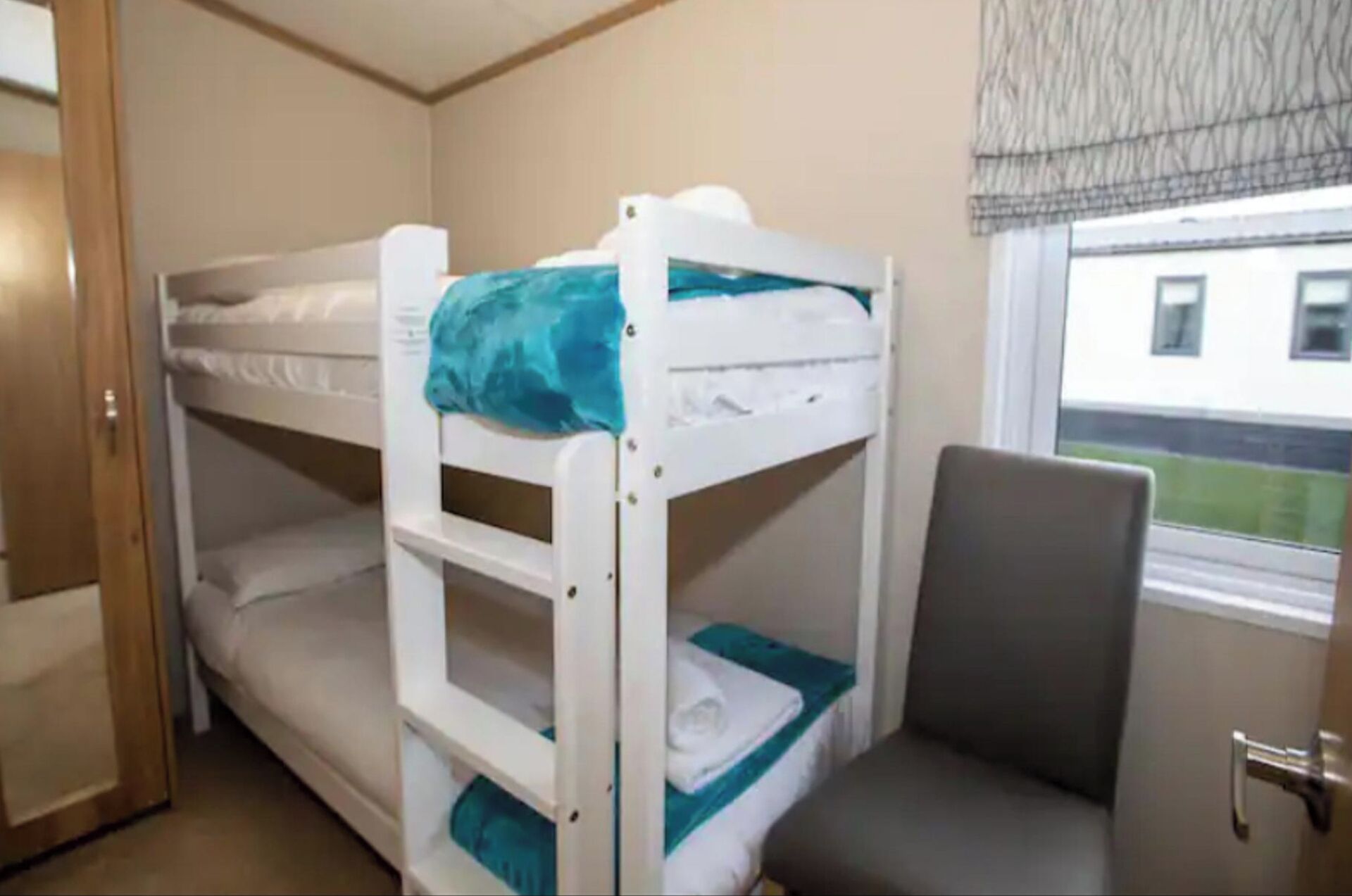 A bunk bed room with a window and a chair.