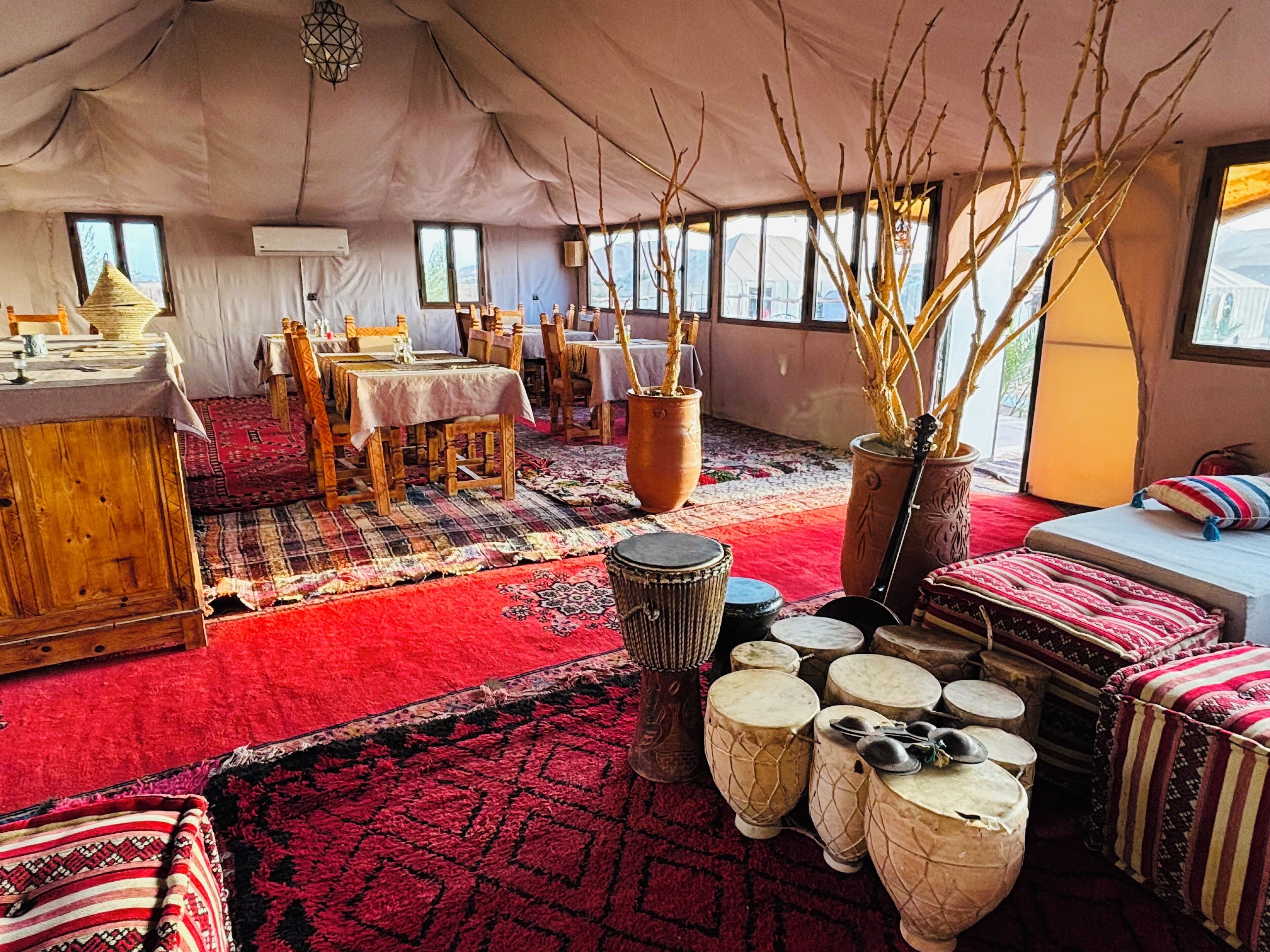 A tented accommodation with a dining area, multiple tables, chairs, and a variety of drums.