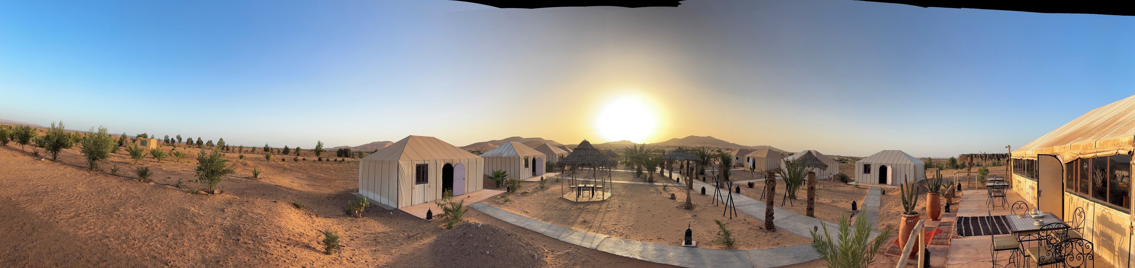 A desert landscape with multiple tents and a central structure with a thatched roof.