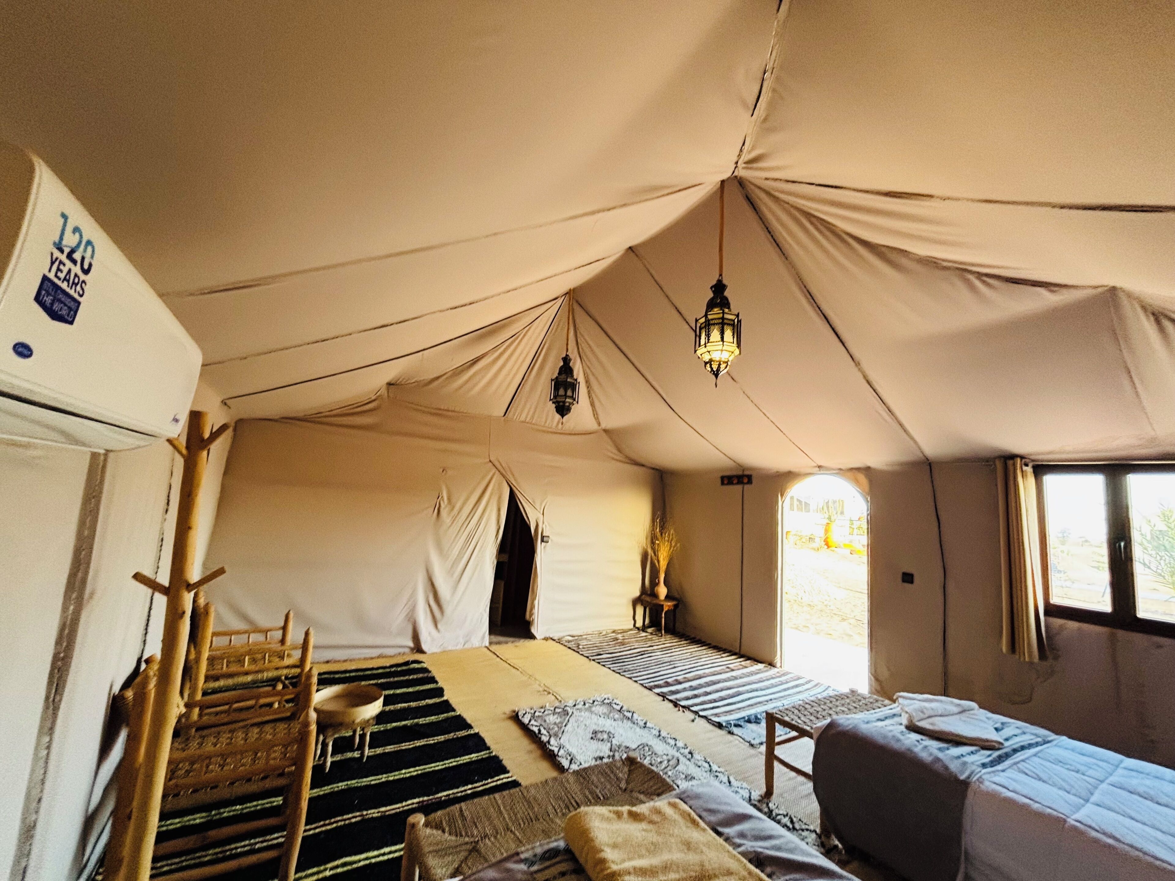 A tented room with a bed, a chair, a table, and a hanging light fixture.