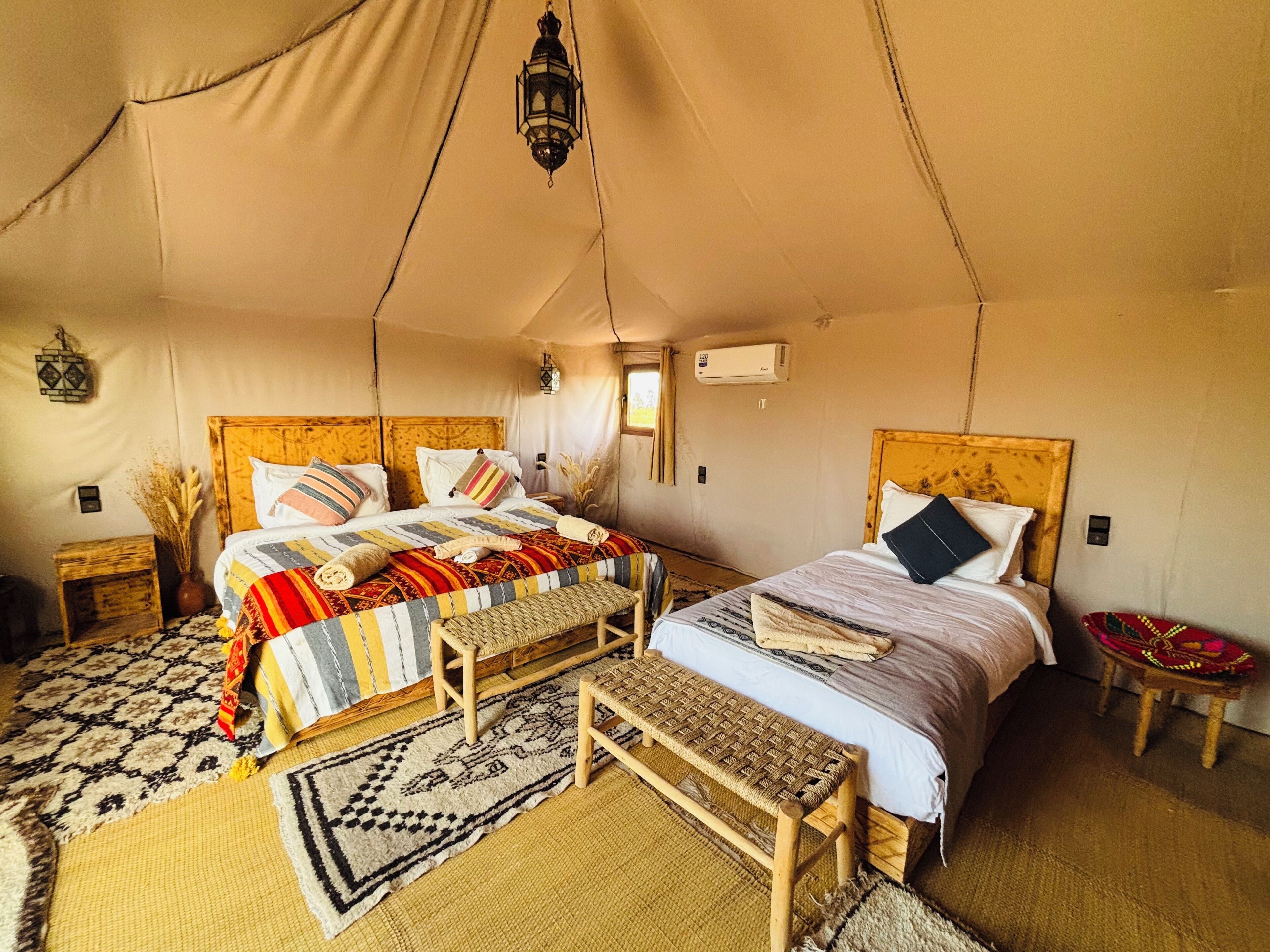A tented accommodation with two beds, a bench, and a small table.
