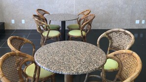 Une table ronde dont le plateau est en granit moucheté, entourée de six chaises en osier avec des coussins verts.